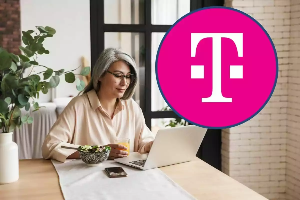 Mujer con cabello canoso y gafas trabajando en una computadora portátil mientras sostiene un vaso de jugo, con un tazón de ensalada y un teléfono móvil sobre la mesa, junto a un logotipo grande de color rosa. Mujer con cabello canoso y gafas trabajando en una computadora portátil mientras sostiene un vaso de jugo, con un tazón de ensalada y un teléfono móvil sobre la mesa, junto a un logotipo grande de color rosa.