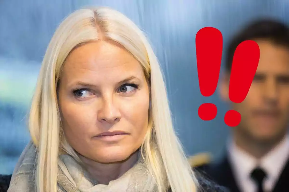 Mette-Marit mira hacia un lado con expresión seria mientras un signo de exclamación rojo aparece al fondo.