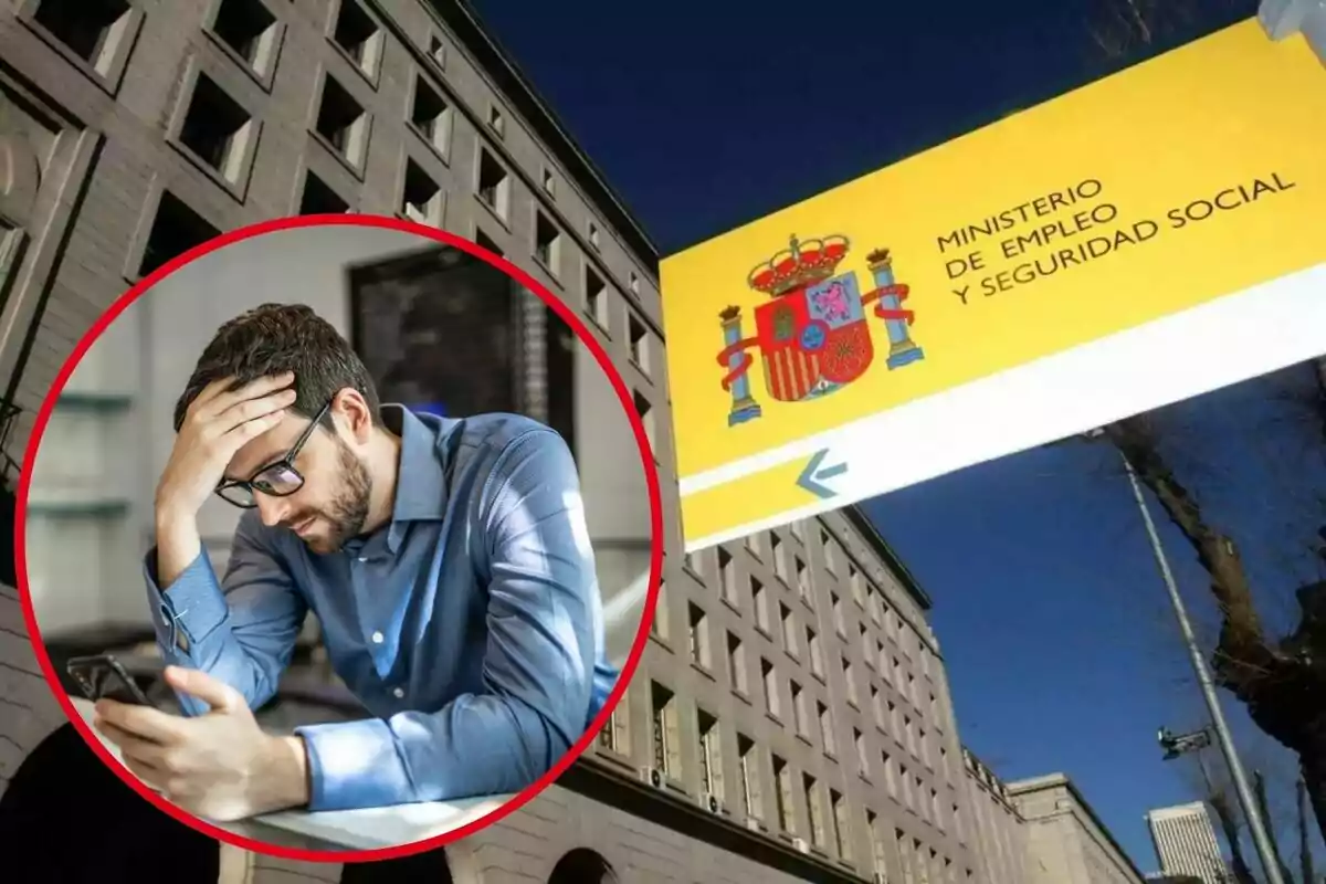 Un hombre con gafas y expresión preocupada mira su teléfono móvil, con un edificio del Ministerio de Empleo y Seguridad Social de España en el fondo.