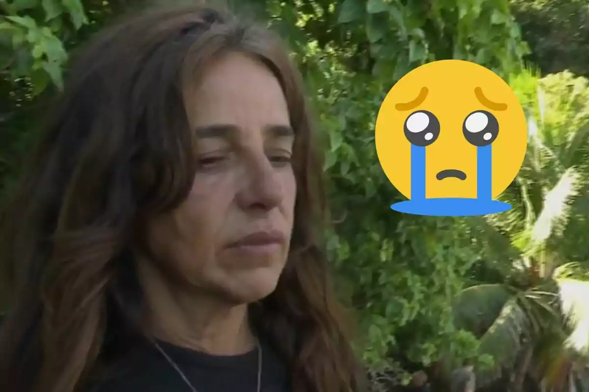 Carmen Alcayde con expresión triste en un entorno natural junto a un emoji grande de carita llorando