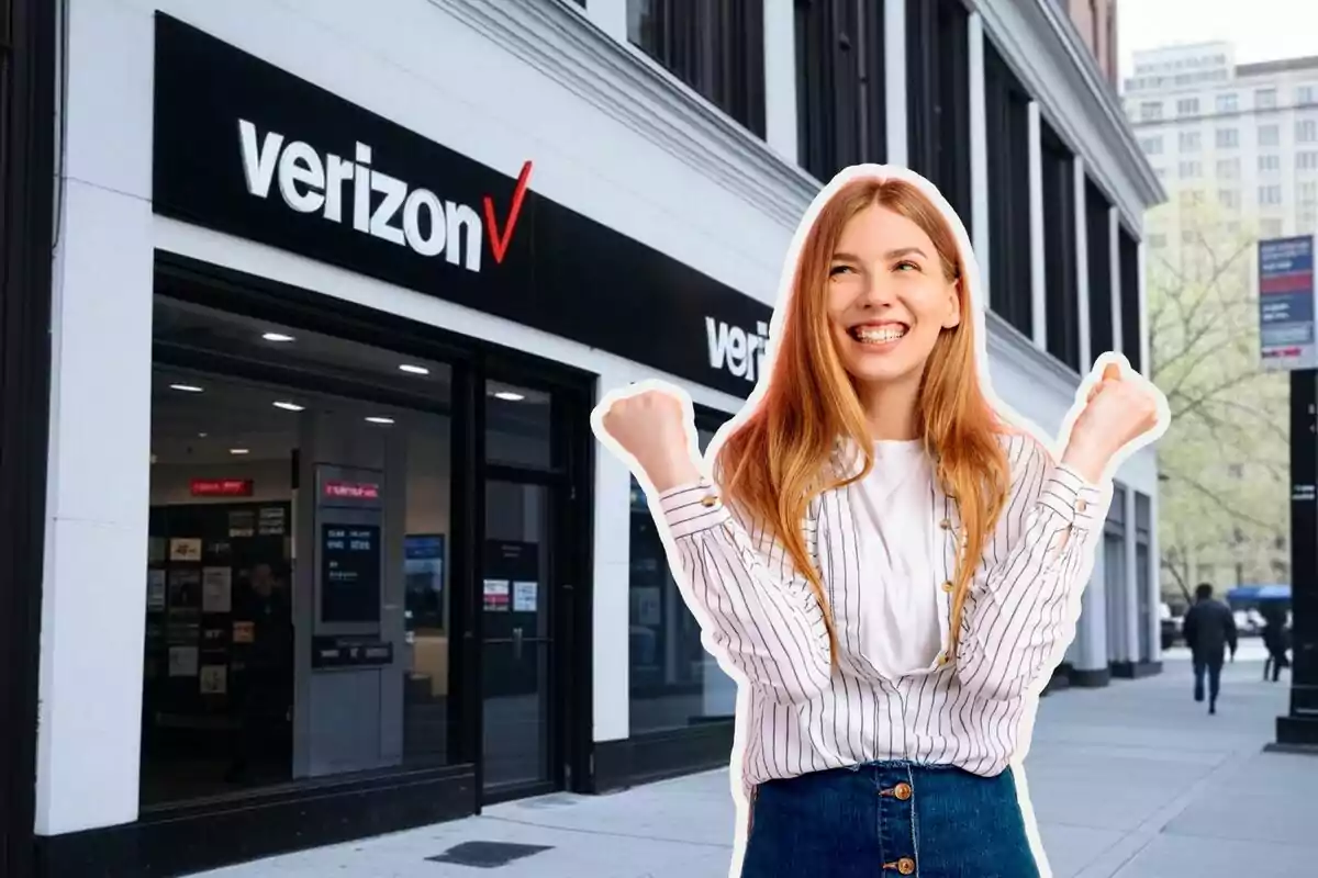 Una mujer sonriente con los puños levantados está frente a una tienda de Verizon en una calle de la ciudad. Una mujer sonriente con los puños levantados está frente a una tienda de Verizon en una calle de la ciudad.