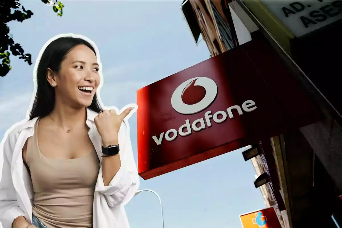 Una mujer sonriente señala un letrero de Vodafone en un entorno urbano.