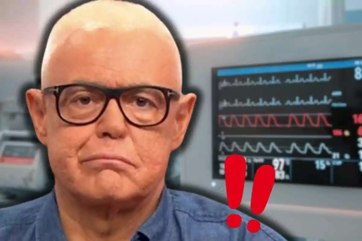 Un hombre con gafas y expresión seria frente a un monitor de signos vitales con signos de exclamación rojos.