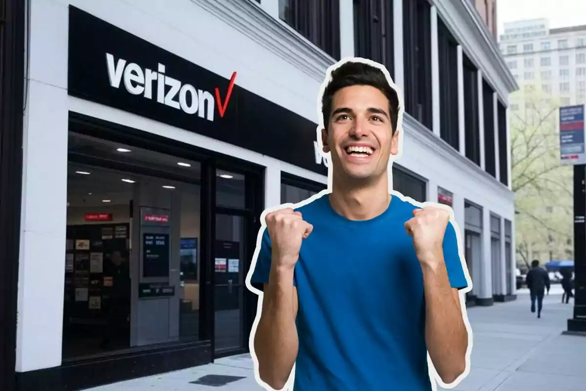 Un hombre sonriente con camiseta azul está frente a una tienda de Verizon. Un hombre sonriente con camiseta azul está frente a una tienda de Verizon.
