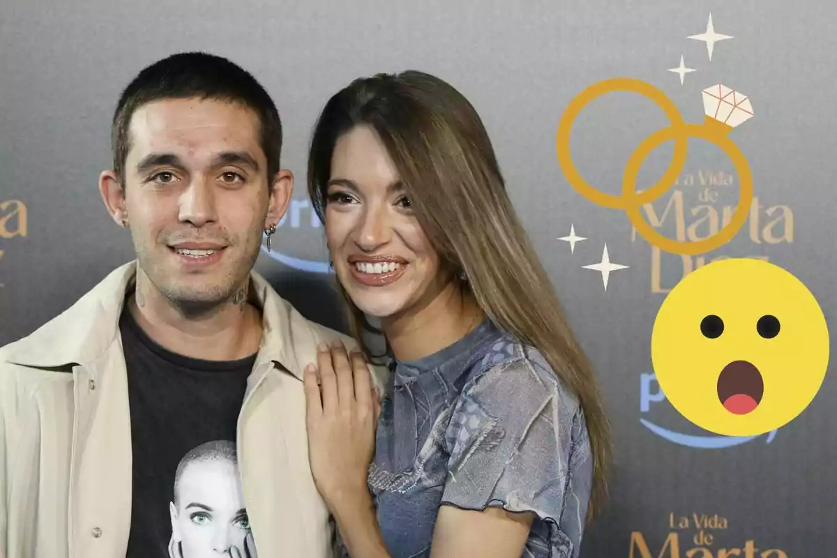 Víctor Elías y Ana Guerra sonriente posa en un evento con un fondo que muestra el título "La Vida de Marta Díaz" y emojis de anillos y una cara sorprendida.