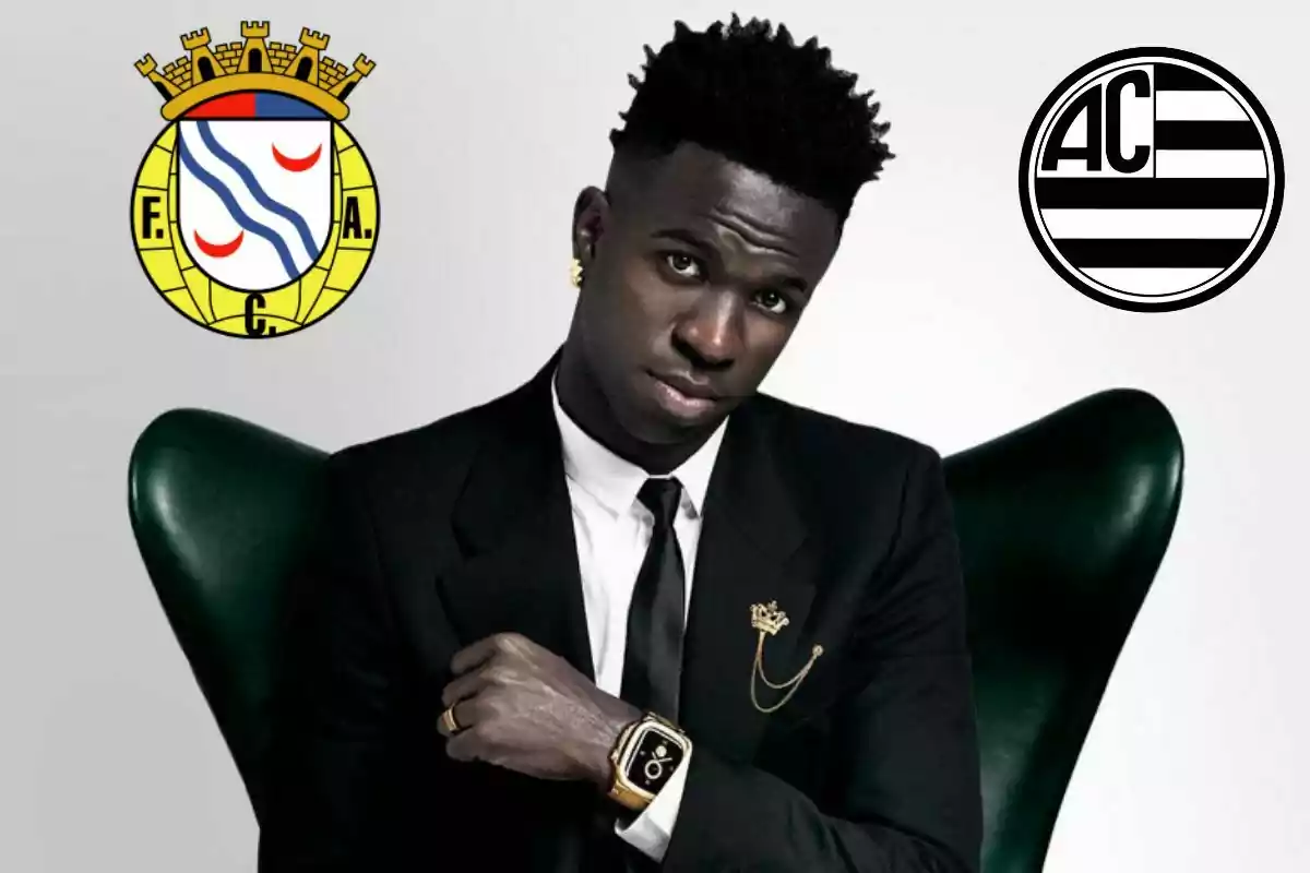 Un hombre con traje negro y corbata posa en una silla verde, lleva un reloj dorado y un pin de corona en la solapa, con dos escudos de fútbol en el fondo.