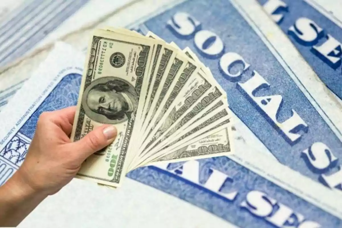 Mano sosteniendo varios billetes de cien dólares sobre tarjetas de seguro social de Estados Unidos Mano sosteniendo varios billetes de cien dólares sobre tarjetas de seguro social de Estados Unidos