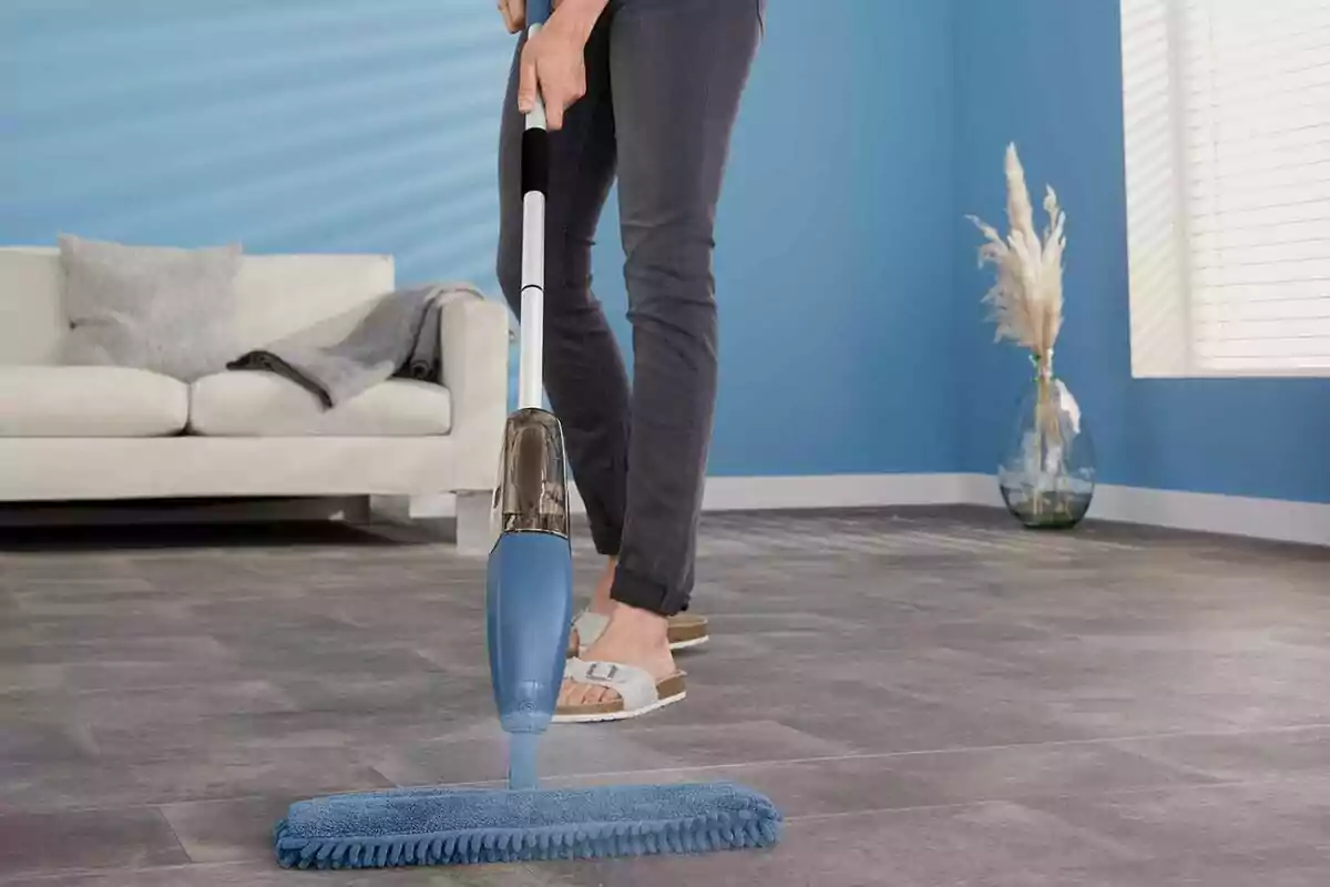 Una persona limpiando el suelo con una mopa de Lidl en una sala de estar moderna con paredes azules y un sofá blanco. Una persona limpiando el suelo con una mopa de Lidl en una sala de estar moderna con paredes azules y un sofá blanco.