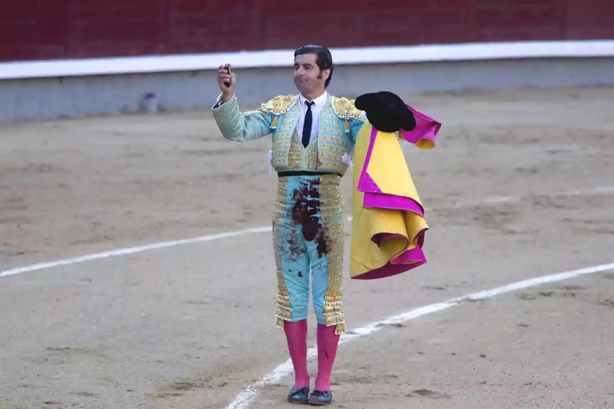 Un torero en la arena sosteniendo un capote y mostrando una oreja como trofeo. Un torero en la arena sosteniendo un capote y mostrando una oreja como trofeo.