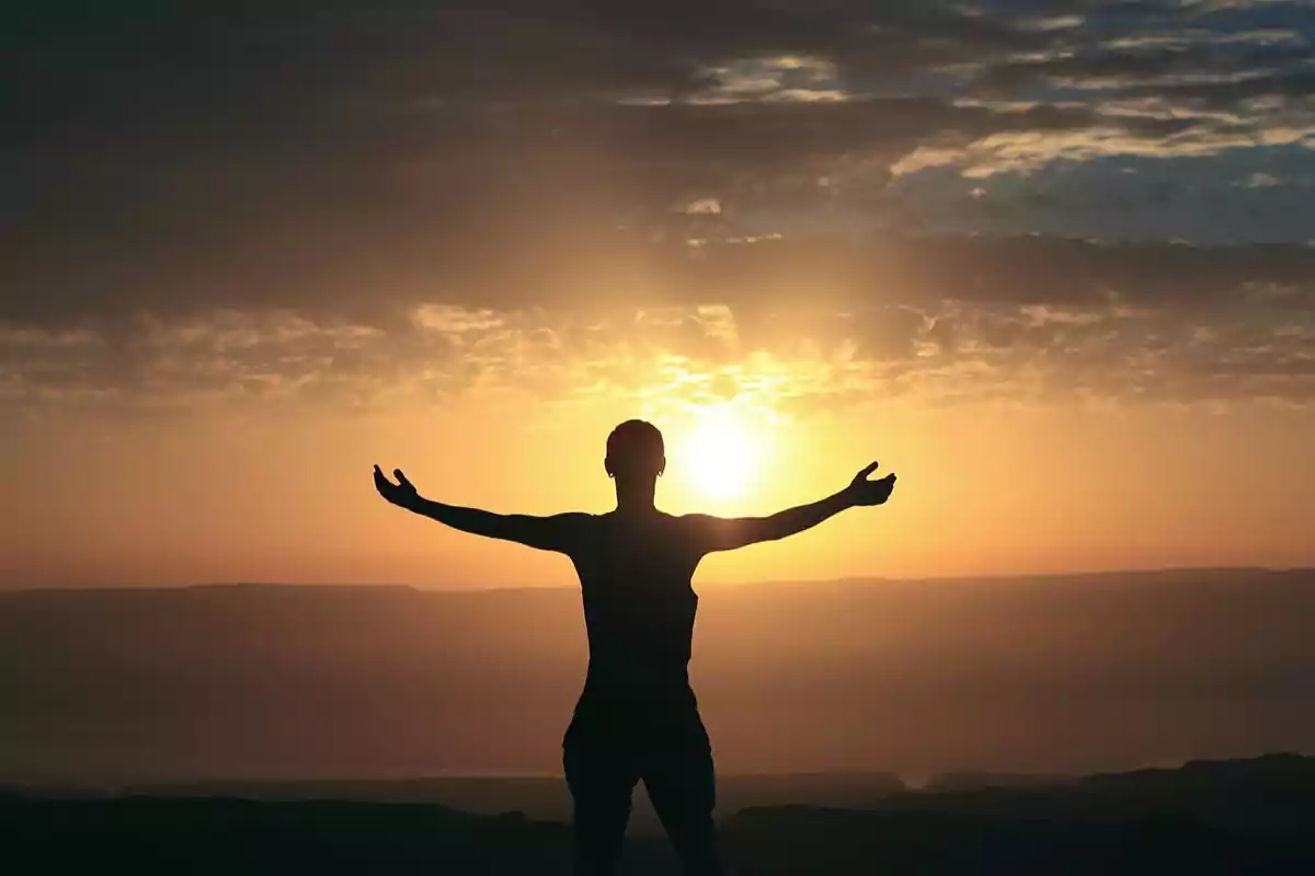 Persona de pie con los brazos extendidos hacia el cielo durante un atardecer.