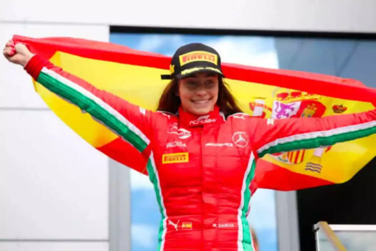 Persona con traje de carreras rojo y gorra negra sosteniendo una bandera de España.