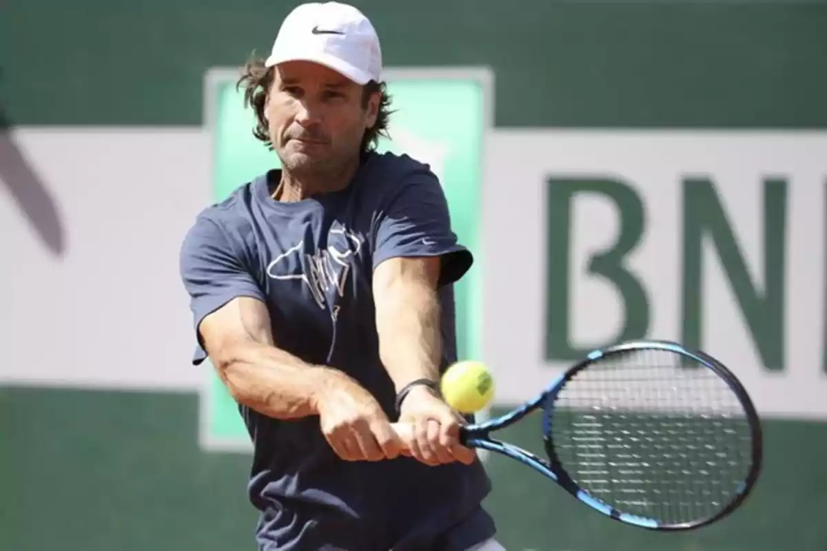 Un hombre jugando al tenis con una gorra blanca y una camiseta azul. Un hombre jugando al tenis con una gorra blanca y una camiseta azul.