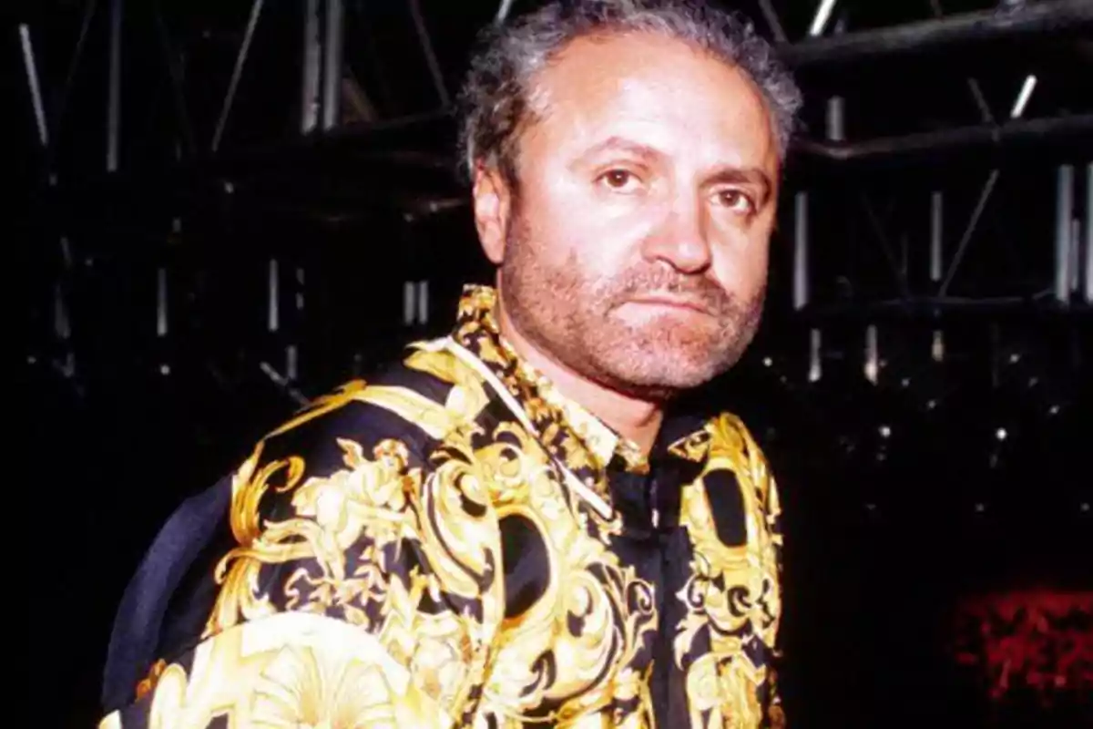 Hombre con camisa de diseño dorado y negro en un entorno oscuro.