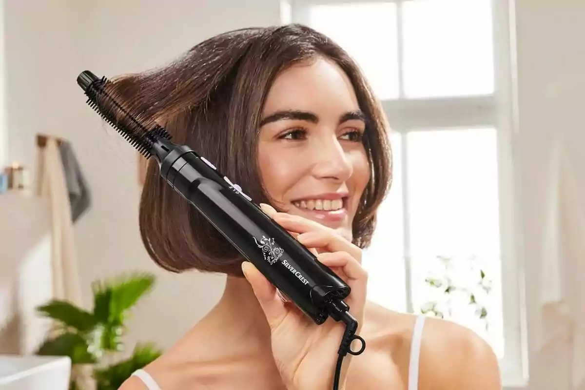 Persona sonriendo mientras usa un cepillo eléctrico de Lidl para peinar su cabello en un baño iluminado. Persona sonriendo mientras usa un cepillo eléctrico de Lidl para peinar su cabello en un baño iluminado.