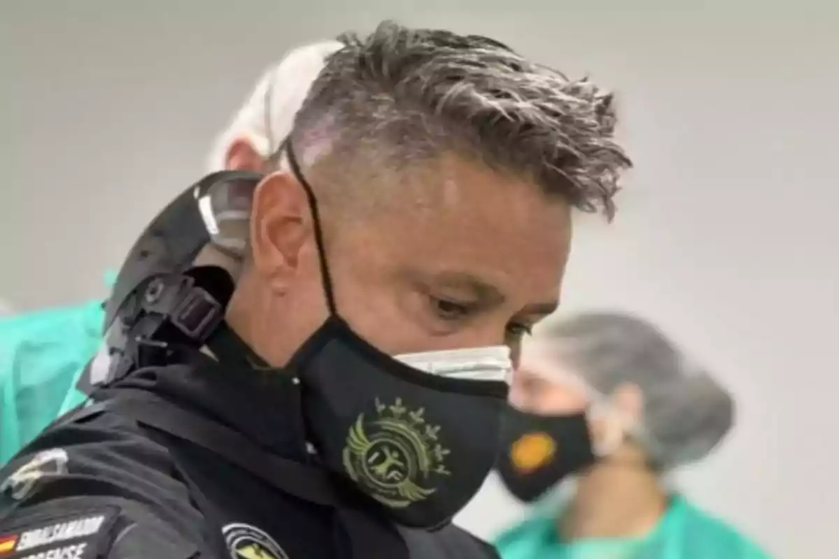 Un hombre con mascarilla negra y uniforme en un entorno médico.