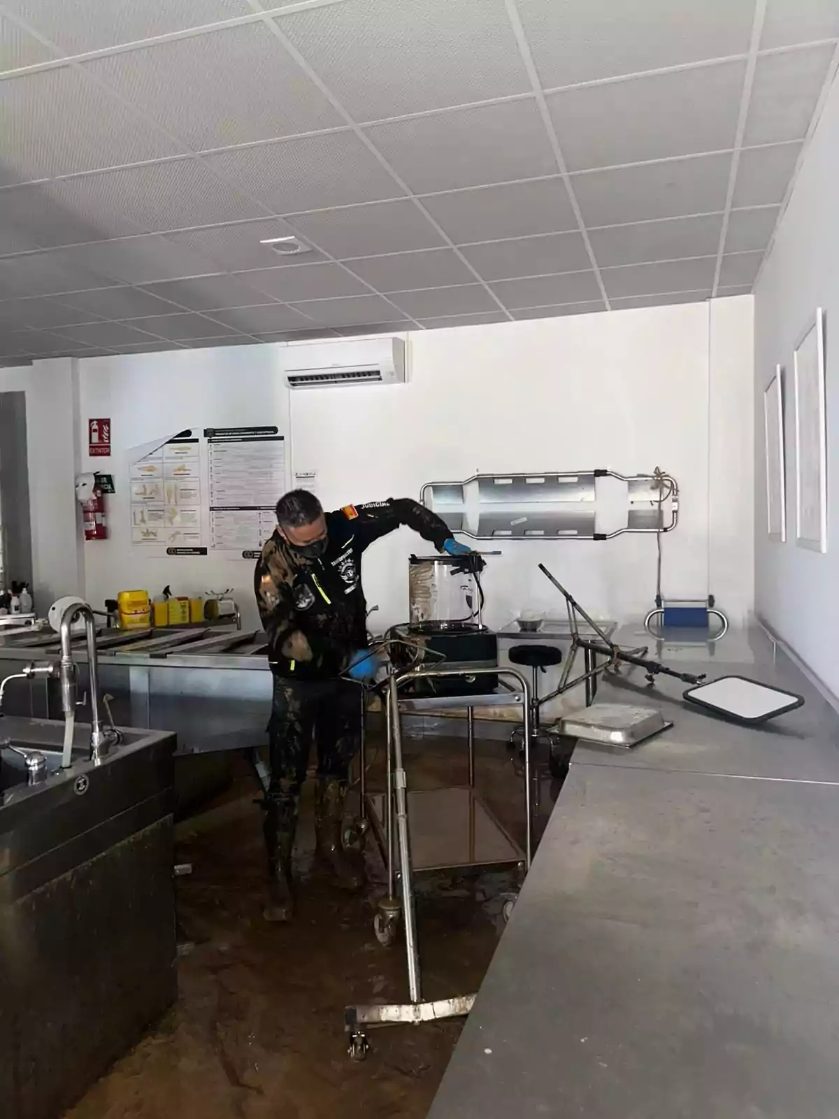 Persona limpiando una sala inundada con equipo de protección y herramientas.