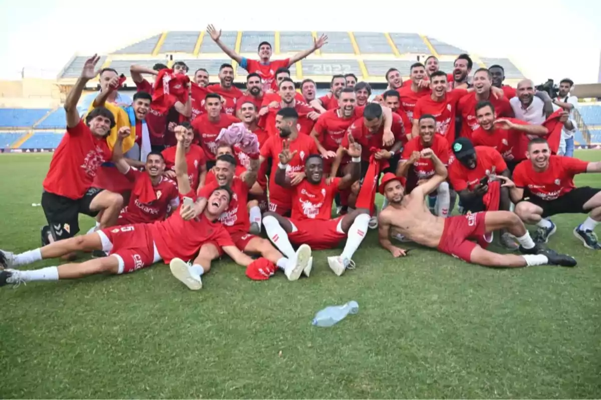 Un grupo de jugadores de fútbol con camisetas rojas celebrando en un campo de fútbol.