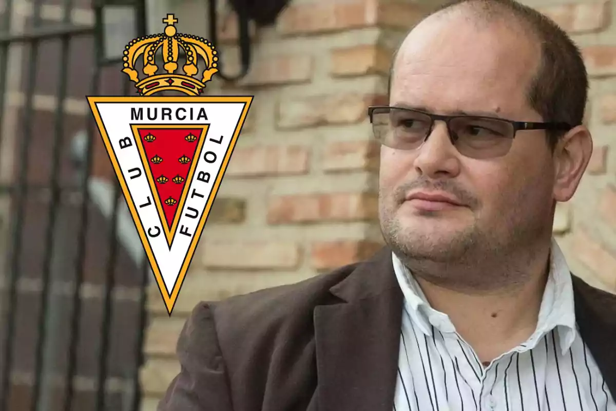 Hombre con gafas y chaqueta oscura junto al escudo del Club de Fútbol Murcia.