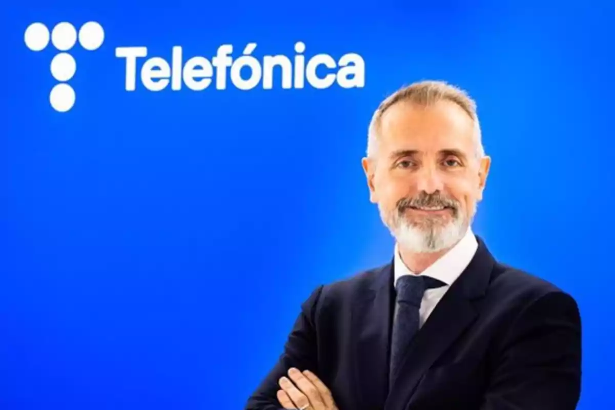 A man in a suit smiles in front of a blue background with the Telefónica logo.