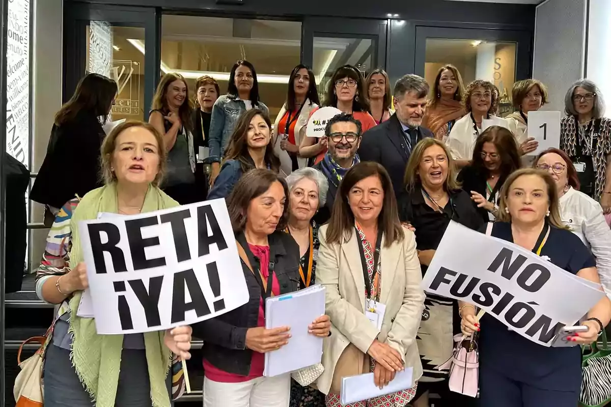 Un grupo de personas se encuentra reunido frente a un edificio, algunas de ellas sostienen pancartas con mensajes como 