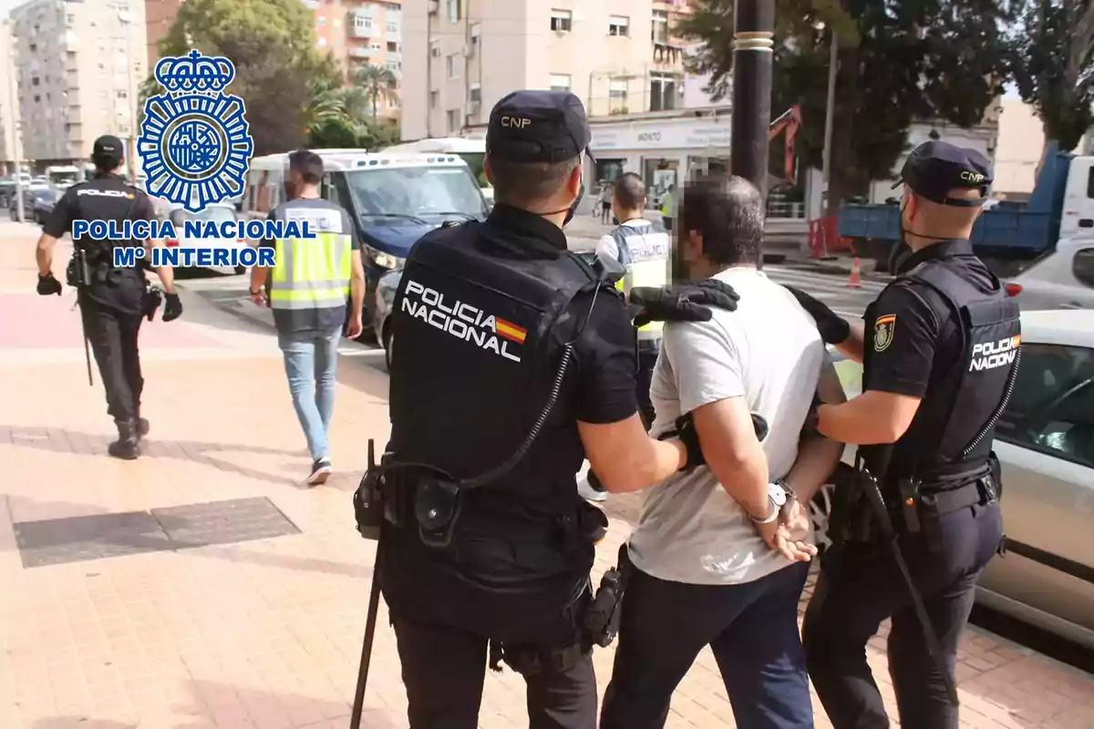 Policías nacionales arrestan a un hombre en una calle urbana mientras otros agentes caminan hacia adelante.