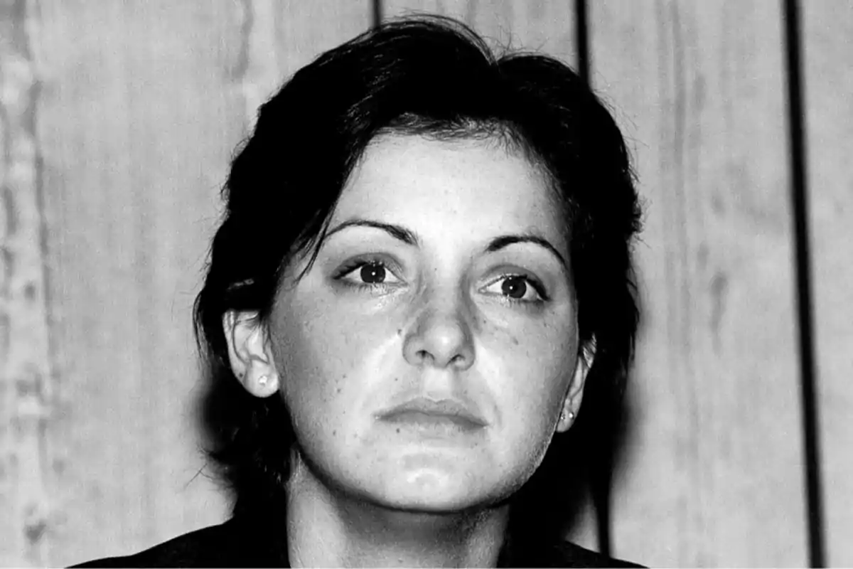 Retrato en blanco y negro de una mujer con expresión seria y cabello corto frente a un fondo de madera.