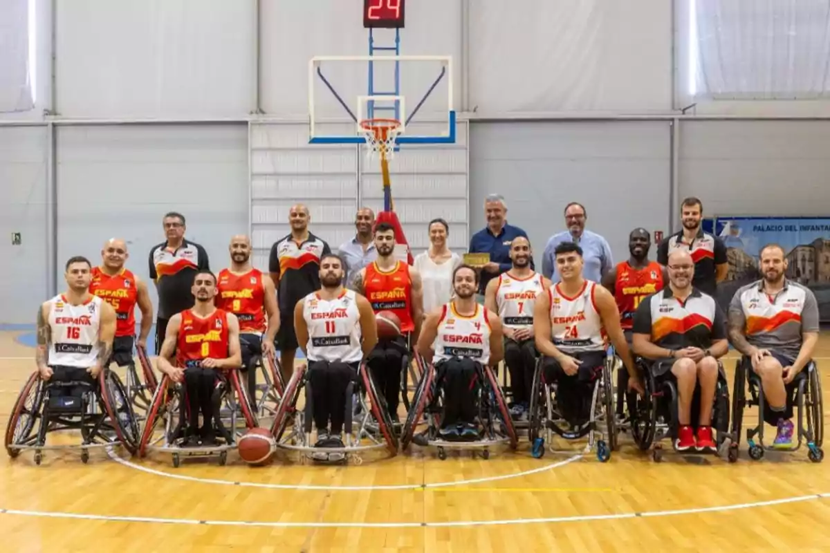 Un equipo de baloncesto en silla de ruedas posa para una foto grupal en una cancha de baloncesto, con jugadores y entrenadores vistiendo uniformes de España.