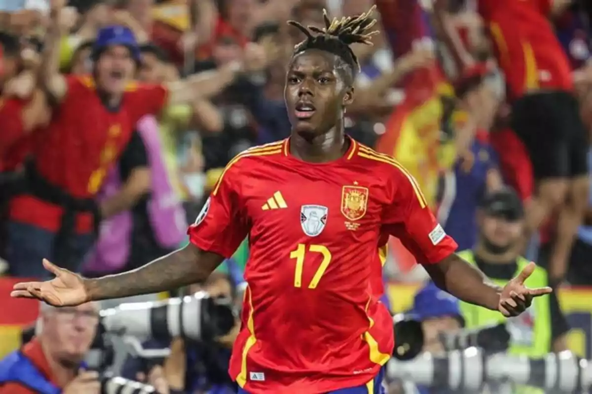 Futbolista con uniforme rojo de la selección de España celebrando un gol con los brazos abiertos frente a una multitud y fotógrafos en el estadio Futbolista con uniforme rojo de la selección de España celebrando un gol con los brazos abiertos frente a una multitud y fotógrafos en el estadio