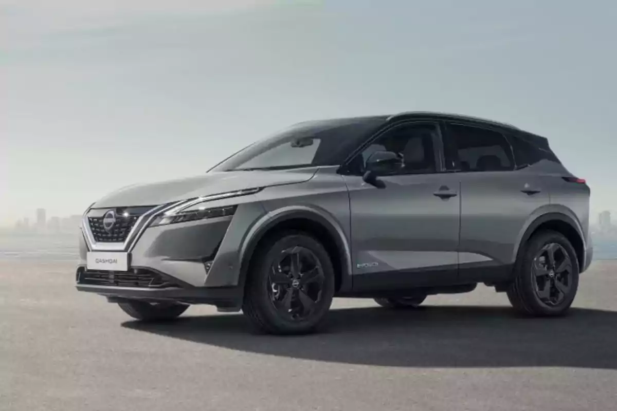 nissan quasqai epower tekna 2023 gris estacionado en un área abierta con una ciudad de fondo.