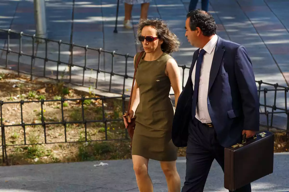 Dos personas caminando por la calle, una mujer con vestido verde y un hombre con traje azul y maletín.