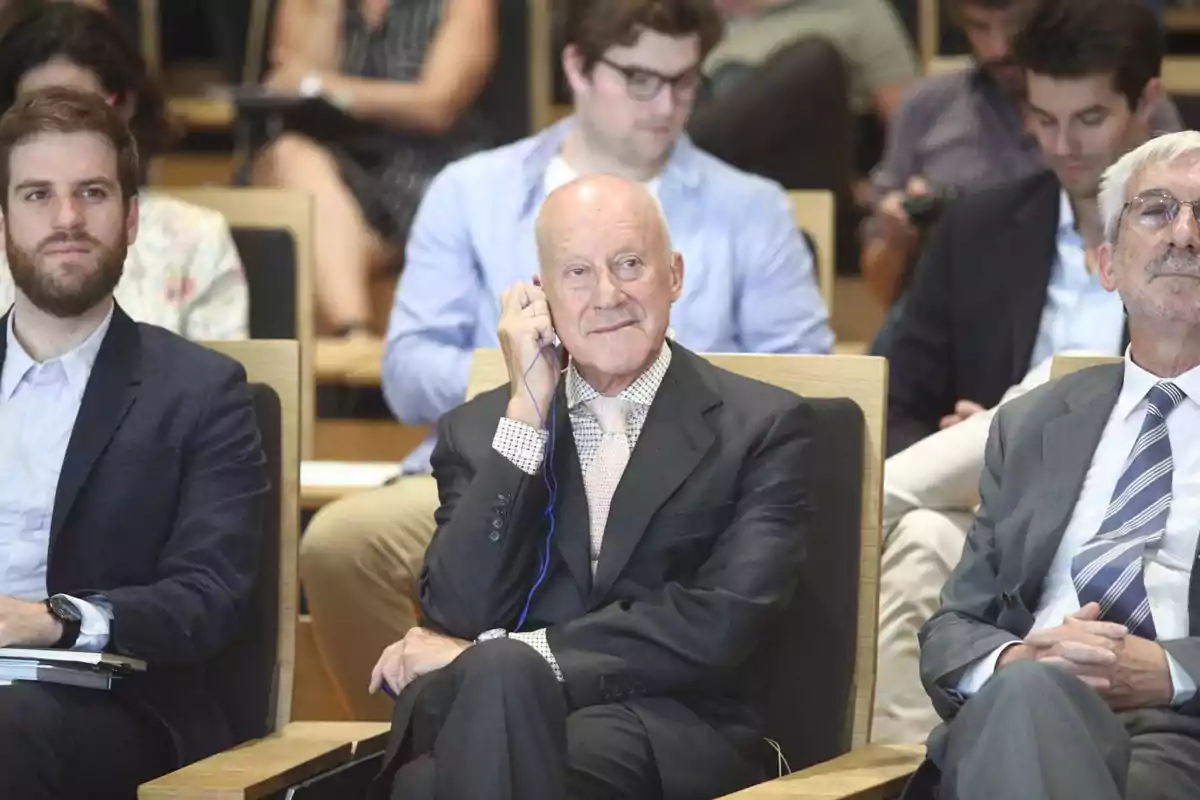 Hombres sentados en una conferencia con público al fondo Hombres sentados en una conferencia con público al fondo