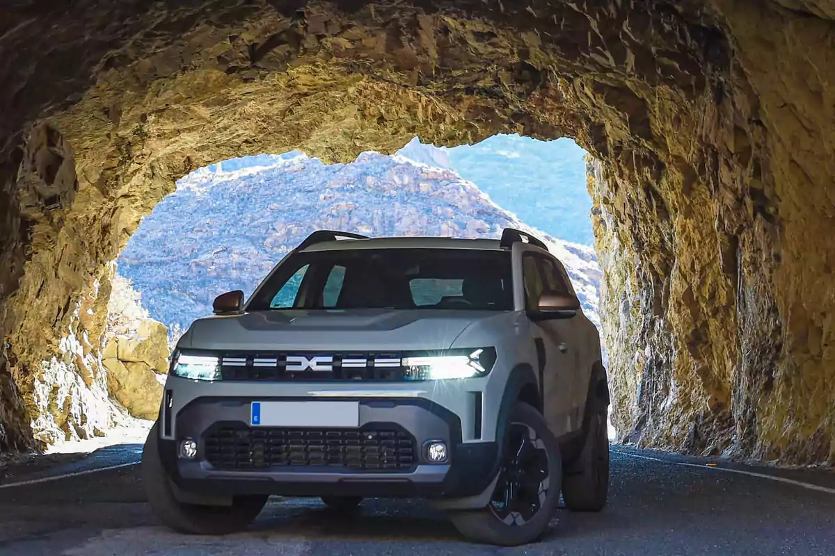 Un SUV gris estacionado en la entrada de un túnel de roca con montañas al fondo
