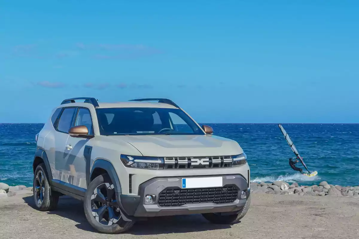 SUV estacionada junto al mar con una persona practicando windsurf en el fondo SUV estacionada junto al mar con una persona practicando windsurf en el fondo
