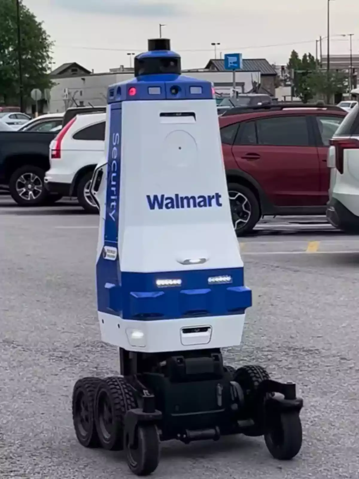 Robot de seguridad autónomo de Walmart patrullando un estacionamiento entre varios autos Robot de seguridad autónomo de Walmart patrullando un estacionamiento entre varios autos