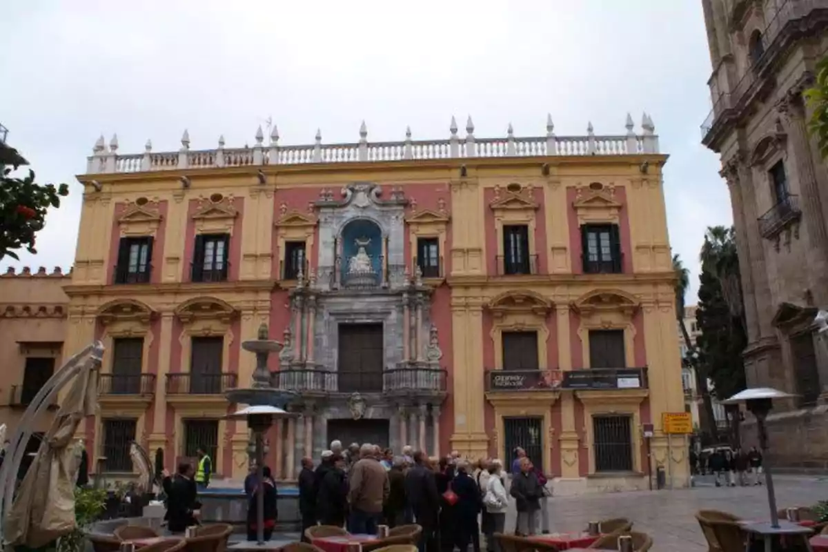 Un grupo de personas se encuentra reunido frente a un edificio histórico de fachada colorida con detalles arquitectónicos ornamentados.