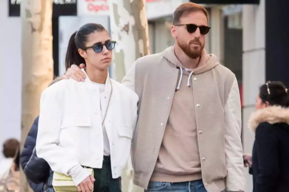Una pareja caminando por la calle, ambos llevan gafas de sol y chaquetas casuales.