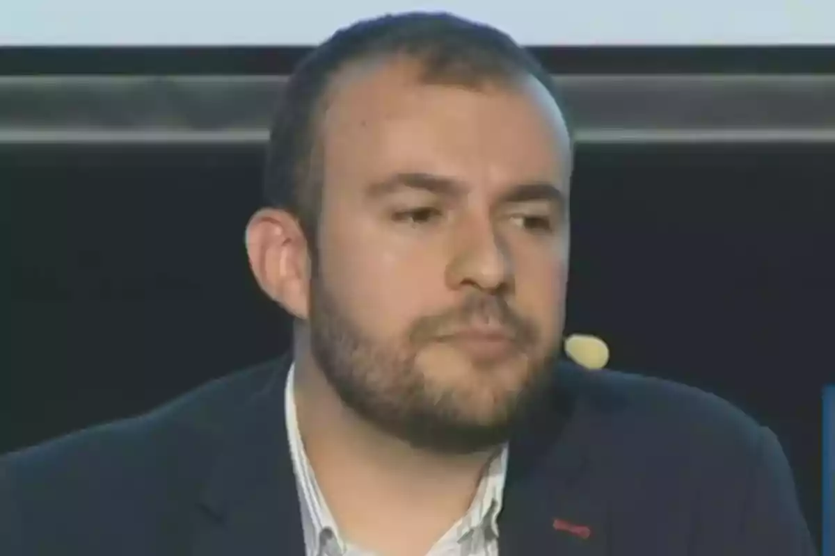 Un hombre con barba y micrófono en una conferencia.