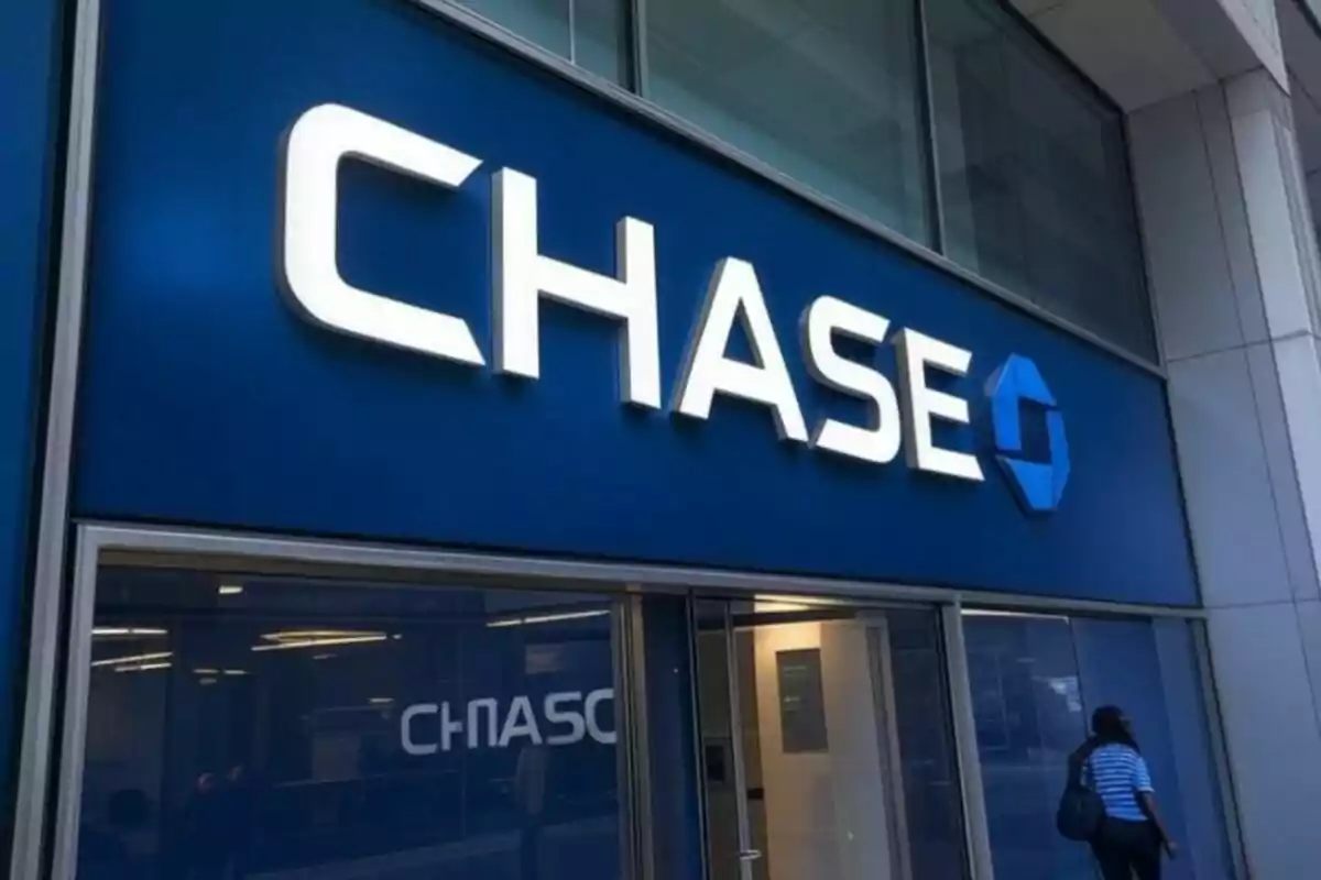 Fachada de una sucursal bancaria con el logotipo de Chase en letras grandes y una persona entrando al edificio. Fachada de una sucursal bancaria con el logotipo de Chase en letras grandes y una persona entrando al edificio.