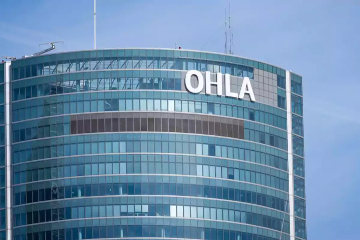 Edificio moderno con fachada de vidrio y el logo de OHLA en la parte superior. Edificio moderno con fachada de vidrio y el logo de OHLA en la parte superior.