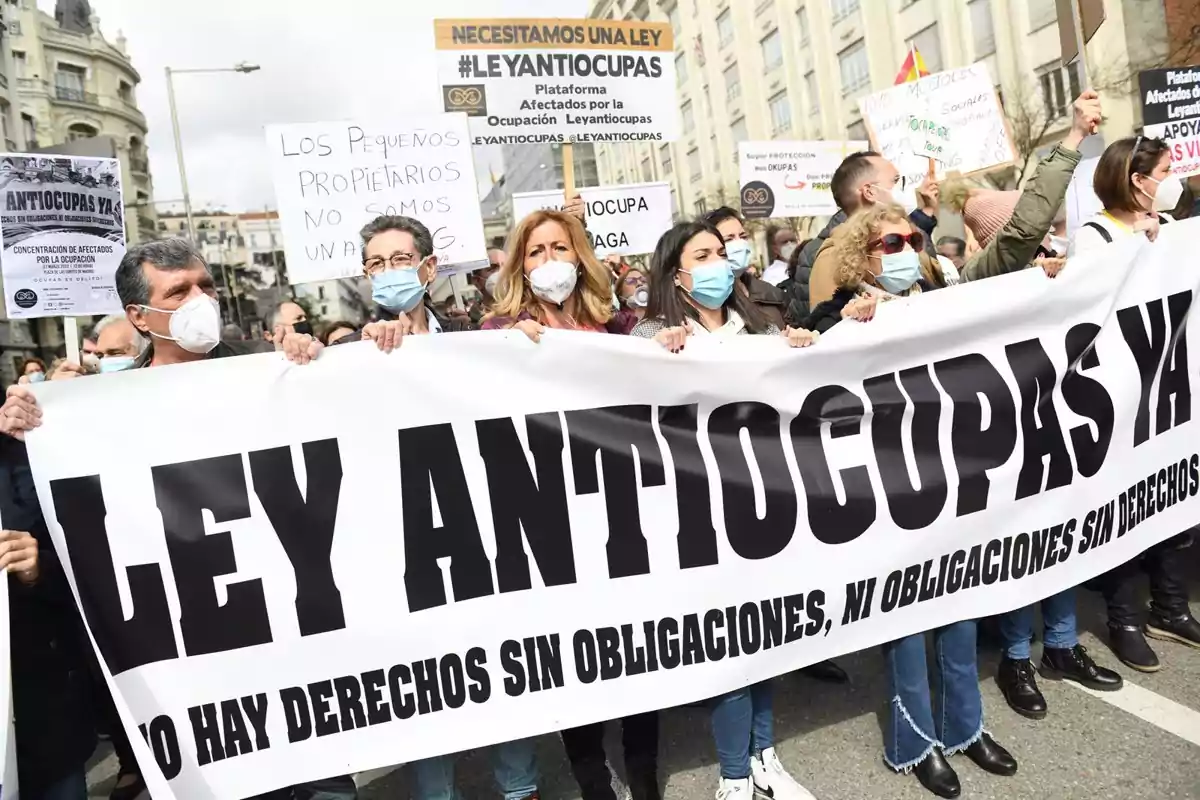 Un grupo de personas se manifiesta en la calle sosteniendo pancartas que exigen una ley contra la ocupación de propiedades.