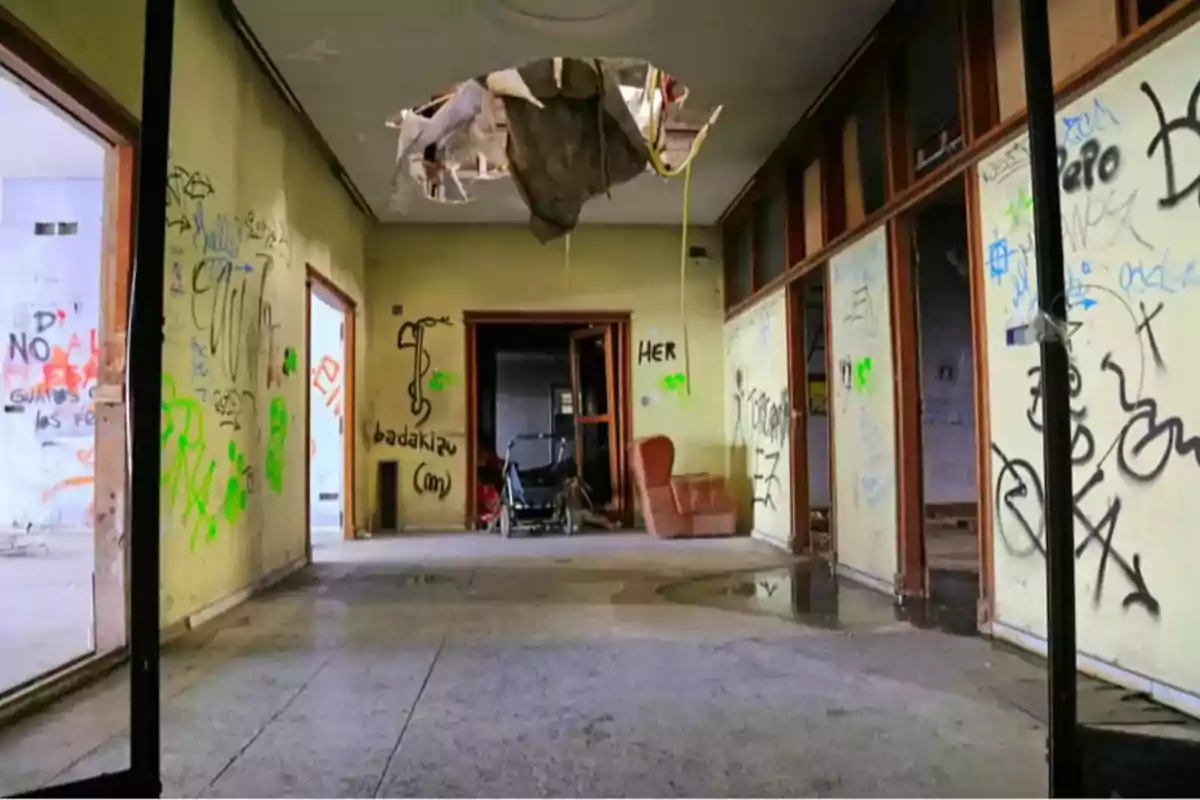 Pasillo de un edificio abandonado con grafitis en las paredes y un agujero en el techo.