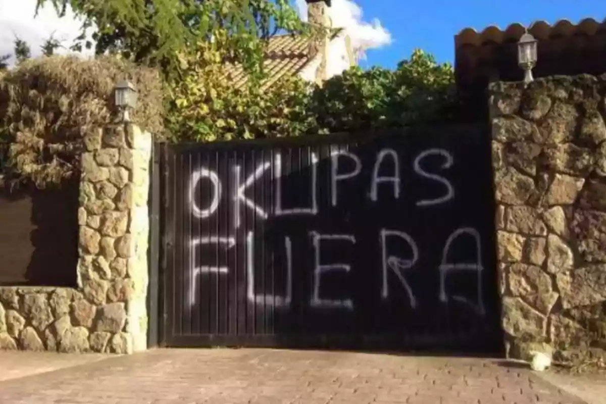 Puerta de metal con grafiti que dice "OKUPAS FUERA" en letras blancas.