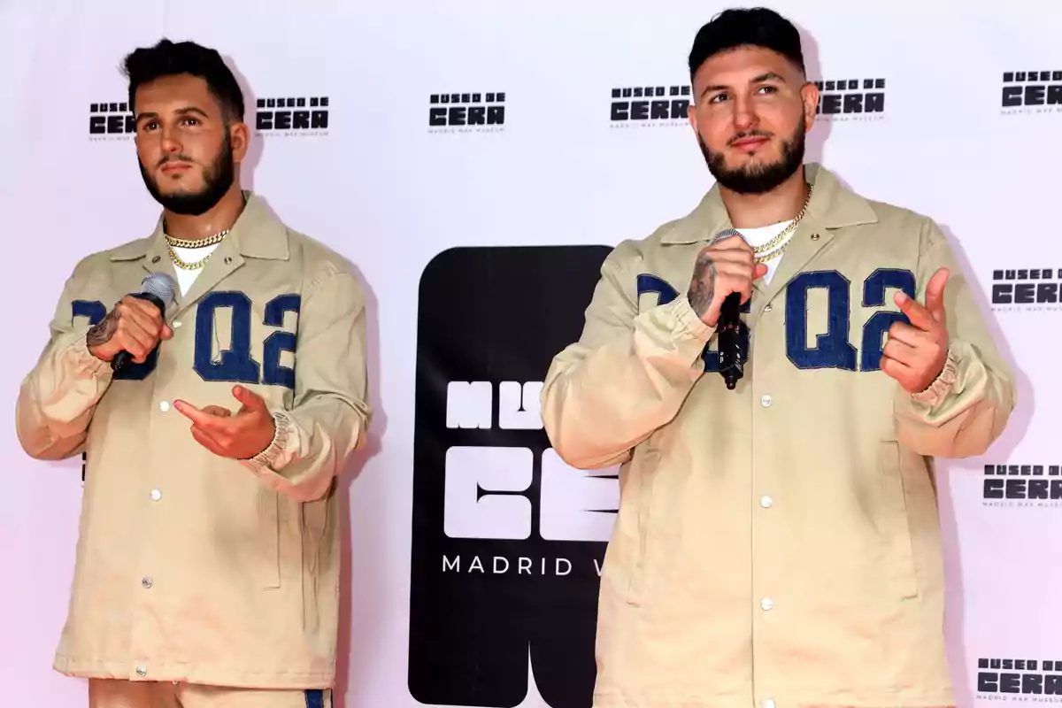 Dos hombres con chaquetas beige y micrófonos posan frente a un fondo con el logo del Museo de Cera de Madrid.