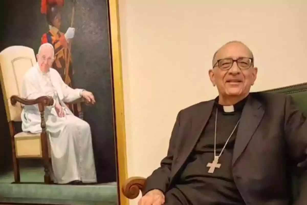 Un hombre con vestimenta clerical y un crucifijo está sentado en una silla junto a un retrato de una figura religiosa en una silla similar.