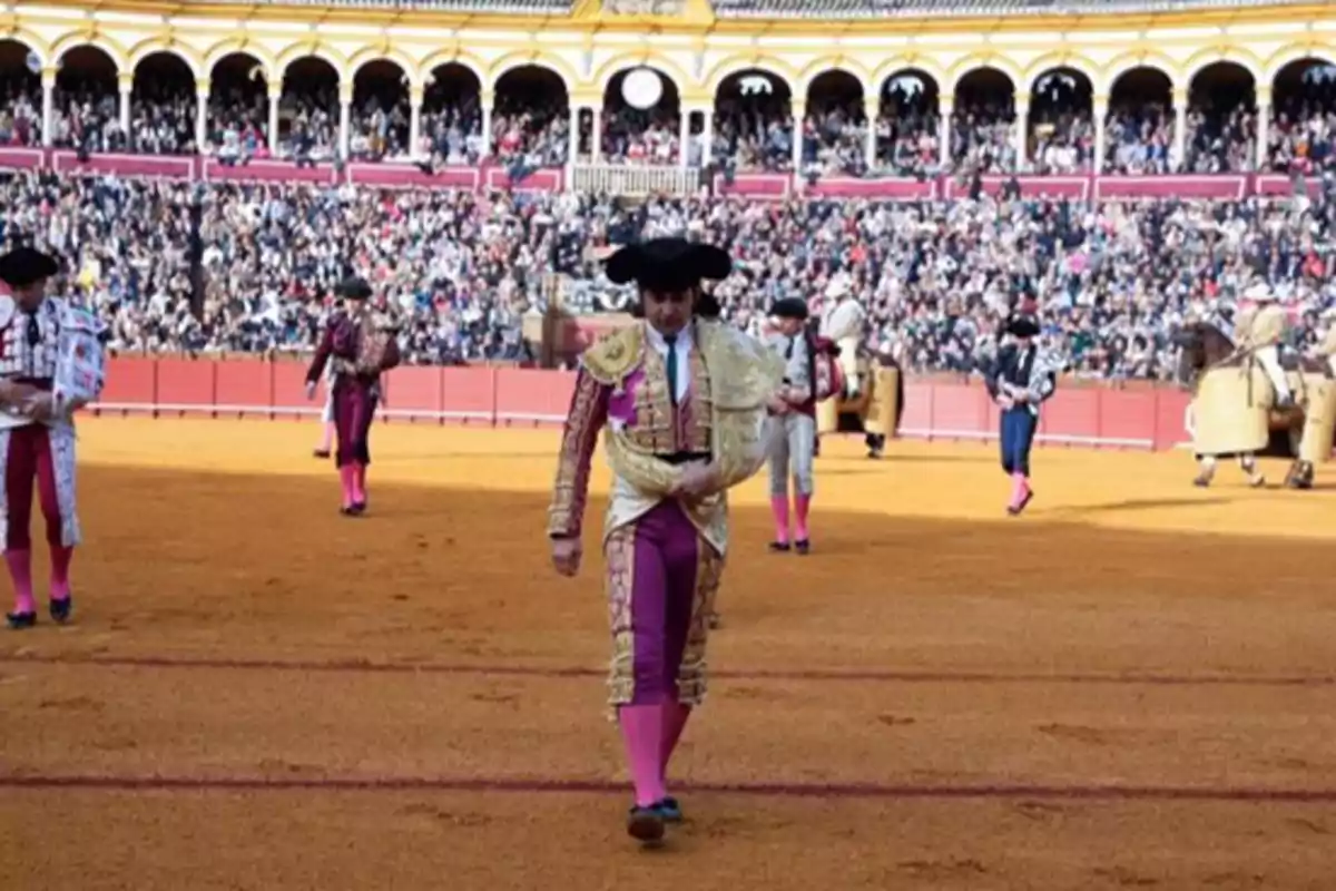 Un grupo de toreros camina en una plaza de toros llena de espectadores.