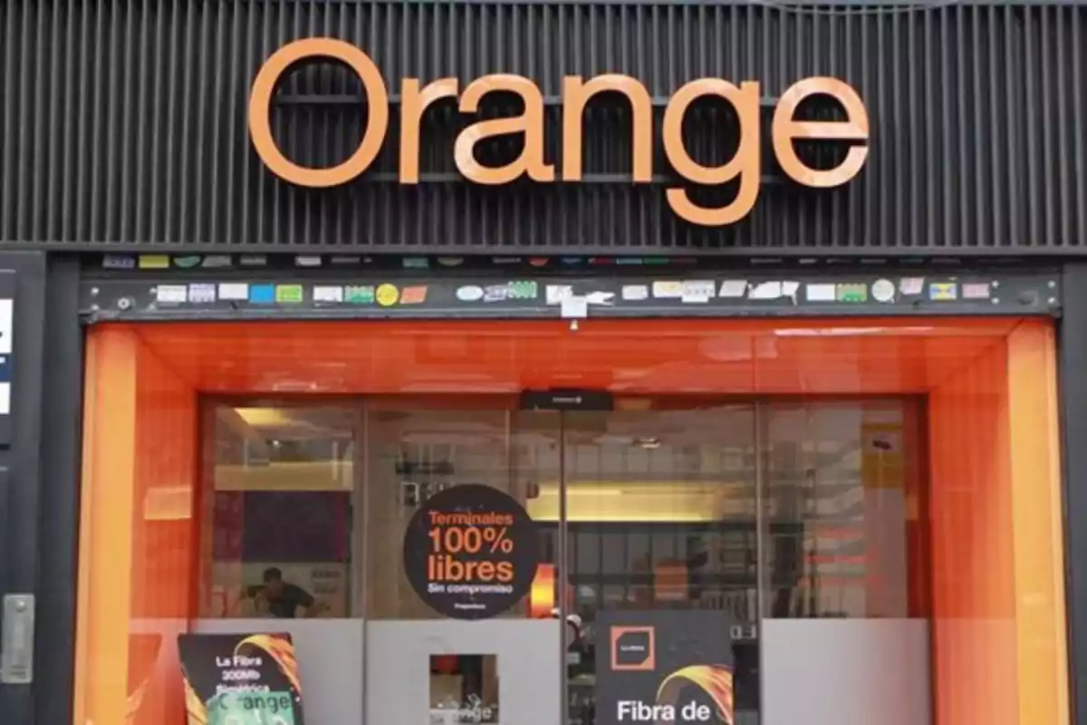 Fachada de una tienda de telecomunicaciones con el logotipo de Orange en la parte superior y carteles promocionales en la entrada. Fachada de una tienda de telecomunicaciones con el logotipo de Orange en la parte superior y carteles promocionales en la entrada.