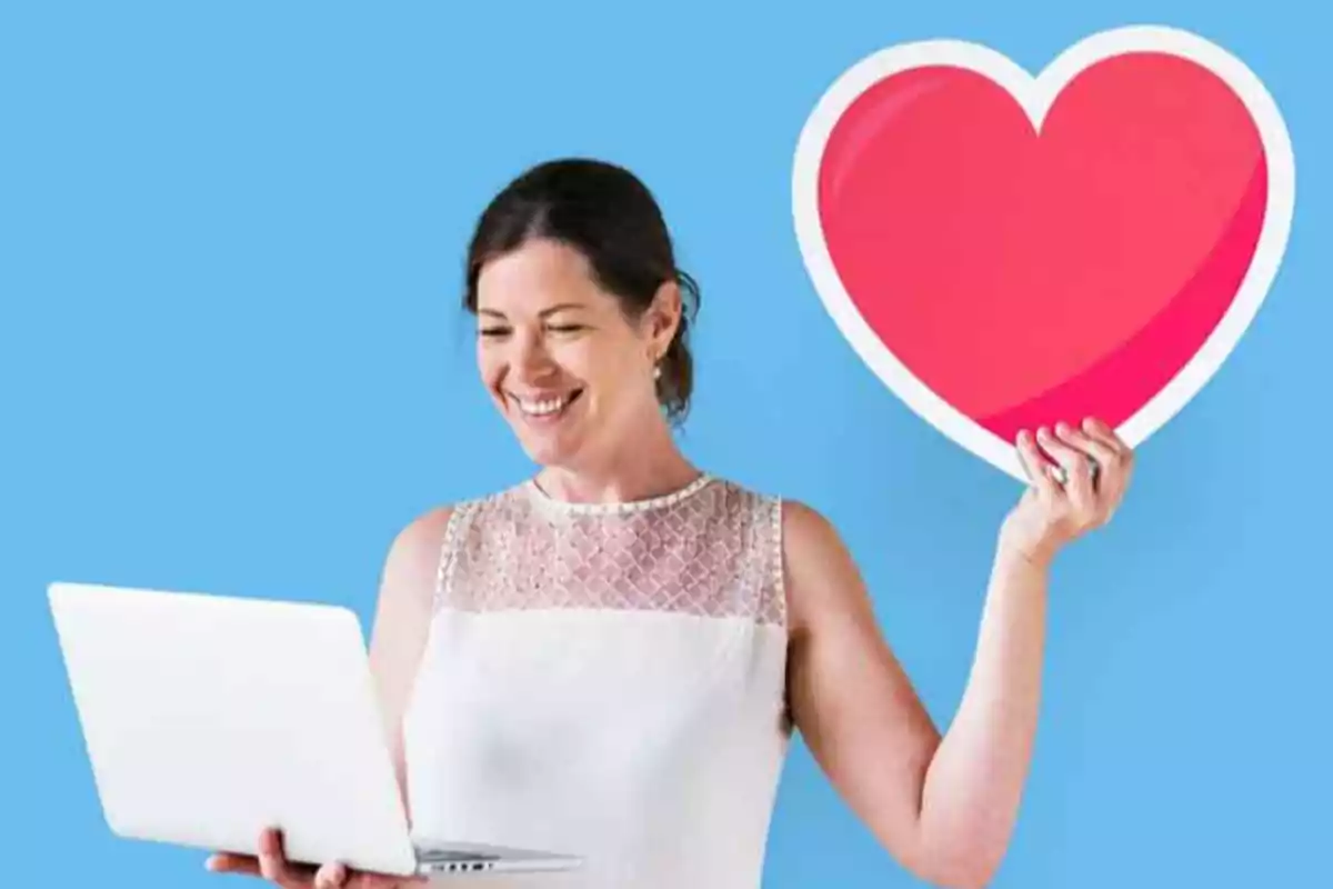 Mujer sonriendo mientras sostiene una computadora portátil y un gran corazón rojo sobre un fondo azul.