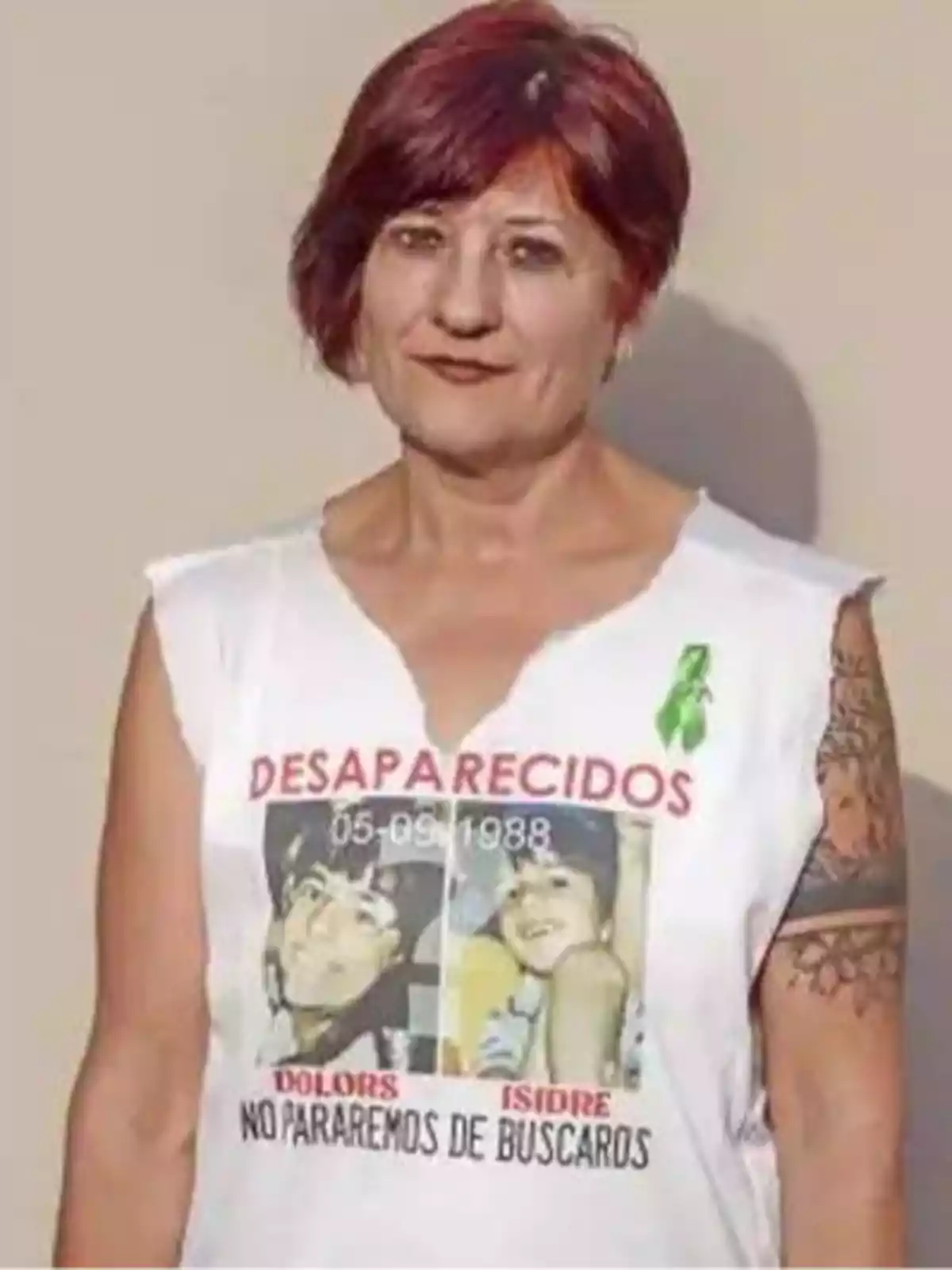 Una mujer con cabello corto y rojo, usando una camiseta blanca sin mangas con fotos y texto que dice 