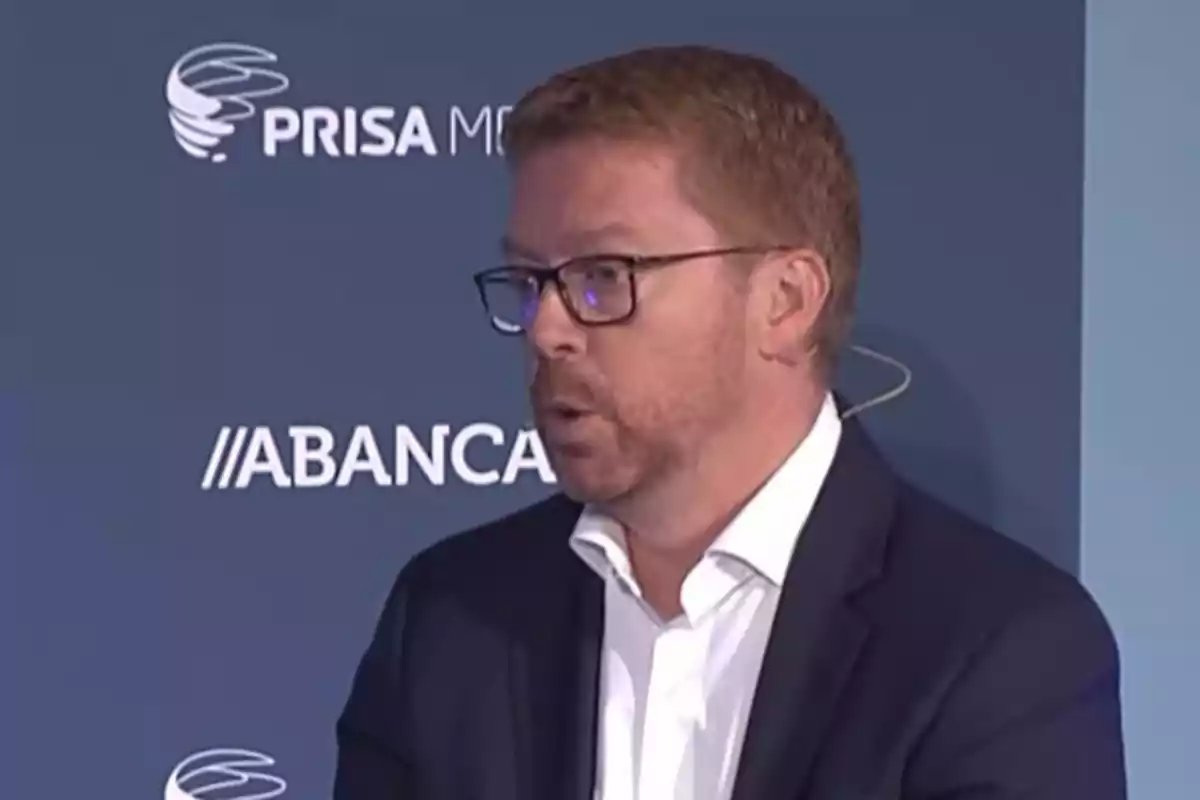 Un hombre con gafas y barba hablando en un evento con logotipos de PRISA Media y ABANCA en el fondo.