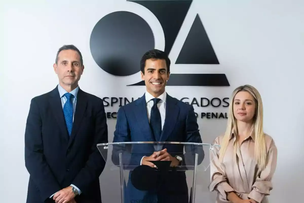 Tres personas vestidas de manera formal posan frente a un atril transparente con un logotipo y el nombre de un despacho de abogados al fondo